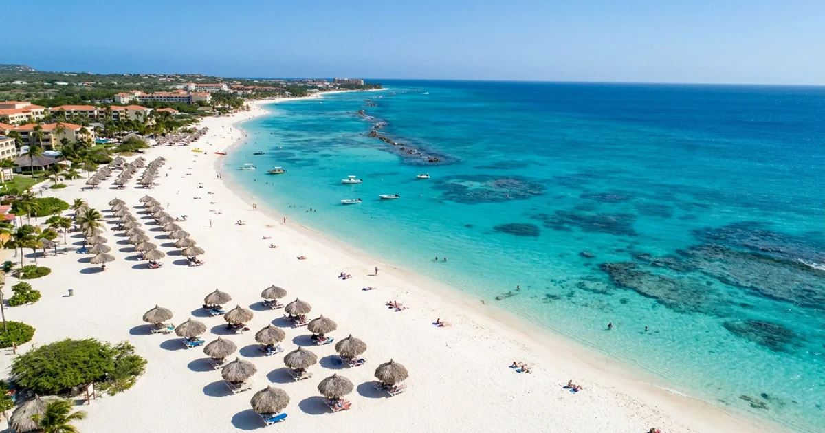 Vista aérea de Eagle Beach em Aruba, com areia branca e fina, mar caribenho de um azul-turquesa cristalino e alguns guarda-sóis de palha.