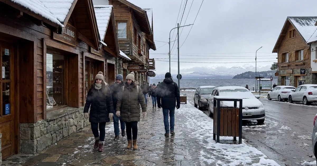 Rua de Bariloche no inverno com neve leve, pessoas caminhando e montanhas ao fundo