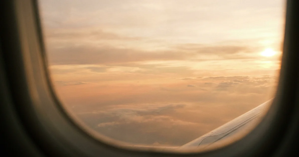 Vista do pôr do sol pela janela de um avião com nuvens alaranjadas