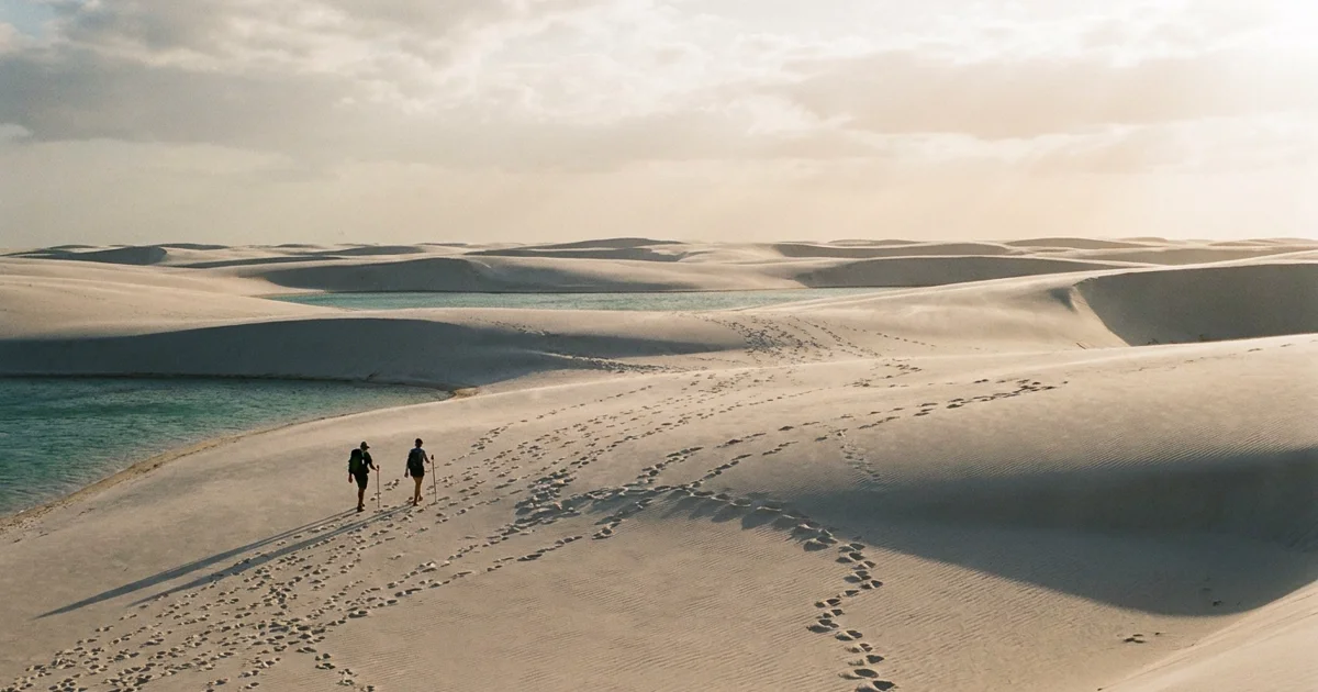 Viajantes caminhando por dunas brancas perto de lagoas nos Lençóis Maranhenses